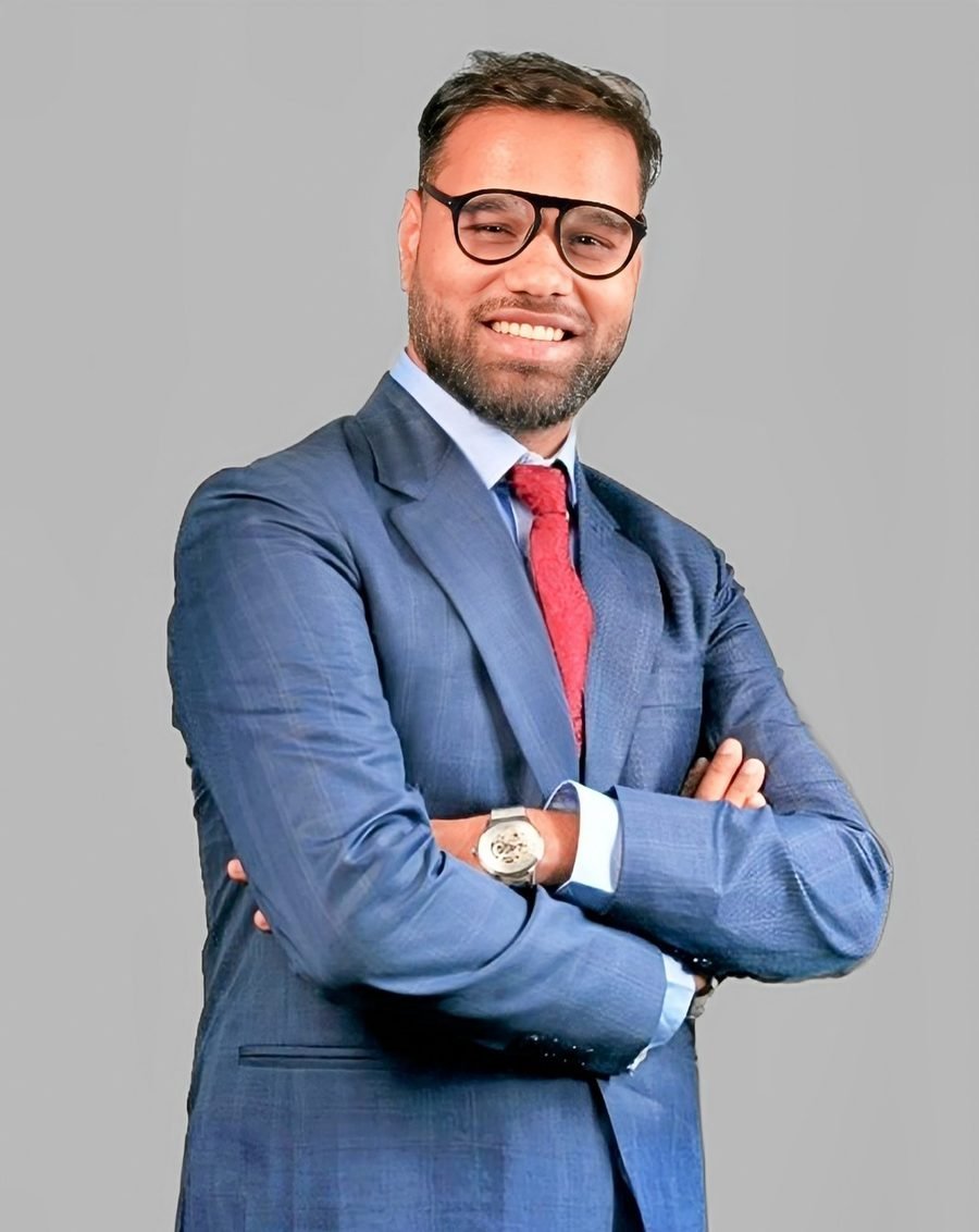 Abhay Jaiswal, smiling, in a blue suit and glasses with arms crossed